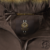 Holland Cooper Cranborne Training Gilet Variant Chocolate. Close-up of a brown puffer jacket interior showing a Holland Cooper brand label on the chest pocket, gold chain detail, faux fur trim, and a tonal embroidered logo on the sleeve.
