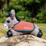 A plush horse toy wearing an orange fleece vest with teal trim and the embroidered brand name 'Le Mieux' on the front, posed outdoors on a rock with a blurred green garden background.