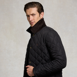 A man wearing a navy diamond-quilted jacket with a dark brown plush collar, posed against a textured light gray background.