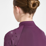 Back view of a woman wearing a purple athletic top with small black embellishments on the shoulders, against a light gray studio background.