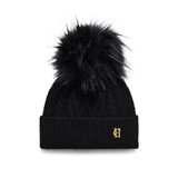 Holland Cooper Sloane Cable Bobble Hat Variant Black. A black cable-knit beanie with a large black faux fur pom-pom and a small gold embroidered monogram logo on the front cuff, shown against a plain white background.