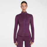 Aztec Diamond AW26 Core Fitted Jacket Variant Plum. A woman modeling a fitted long-sleeve athletic zip-front jacket in a deep plum purple color, paired with matching leggings, against a clean light grey studio background.