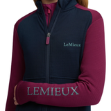 LeMieux AW26 Young Rider Bethany Fleece Zip Through Varient Blackberry. A close-up of a person wearing a LeMieux fleece jacket with navy blue body panels and magenta sleeves, featuring a teal embroidered logo on the chest and a larger matching logo across the sleeve cuff.