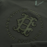 Holland Cooper Cranborne Crystal Crew Variant Ivy Green. Close-up of a dark olive green sweatshirt featuring an embroidered circular 'Holland Cooper Sporting Heritage' monogram logo on the chest.