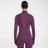 Aztec Diamond AW26 Core Fitted Jacket Variant Plum. A woman viewed from the back wearing a fitted long-sleeve athletic top and matching leggings in a solid deep plum-purple color, against a clean light grey studio background.