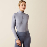Ariat Ladies Lunaveil 1/2 Zip Long Sleeve Base Layer Variant QuickSilver. A woman modeling a light gray long-sleeve athletic quarter-zip top and matching gray leggings against a plain beige studio background.
