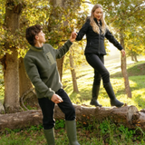LeMieux AW26 Mens Borg Half Zip Sweat Varient Olive. Two people holding hands in a woodland setting. The girl is wearing all black with black wellys and the boy is wearing a Olive fleece and black trousers.