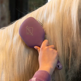 Person using a purple grooming brush on blonde hair with 'LeMieux' branding.