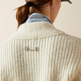 Close-up of a person wearing a textured beige cardigan with a decorative button on a neutral background