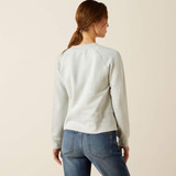 Person wearing a light grey sweatshirt and blue jeans on a beige background