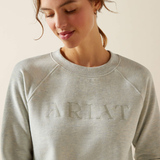 Person wearing a grey sweatshirt with 'Ariat' branding on a plain background