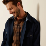 Man wearing a navy jacket over a plaid shirt against a beige background