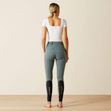 Person wearing green riding pants with 'ARIAT' branding on a plain background