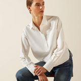 Woman wearing a white shirt and blue jeans sitting on a chair against a beige background