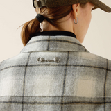 Person wearing a grey checkered coat with a visible brand logo on a beige background