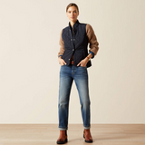 Person wearing a brown knit, navy gilet, blue jeans, and brown boots on a beige background