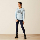 Woman wearing a light blue sweater with a horse design and dark blue leggings on a beige background