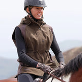 Person riding a horse wearing a brown gilet and helmet with a blurred natural background