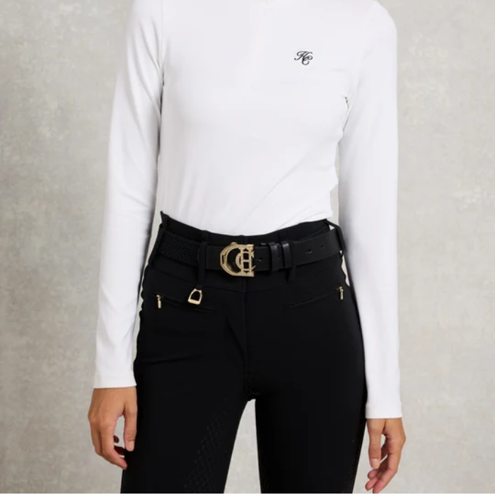 Holland Cooper Stirrup Heritage Belt Variant Colour Black Crystal. A model wearing a white top with 'HC' brand and black leggins with belt with gold clasp, on grey background.