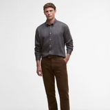 Man wearing a grey button-up shirt and brown trousers on a light grey background