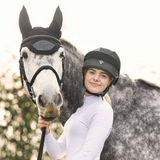 Woman in equestrian gear standing next to a horse with a blurred background