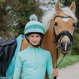 Person in turquoise equestrian gear standing next to a horse outdoors