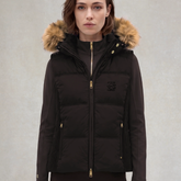 Lady wearing a Brown gilet with a fur hood on a grey background.