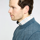 Close-up of a person wearing a blue knitted jumper over a collared shirt on a light background