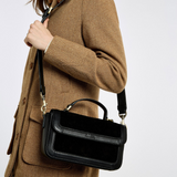 Person wears a brown coat and a black handbag with shoulder strap on a grey background