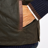 Close-up of a green gilet with a hand in a pocket, wearing a dark sweater.