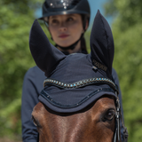 Horse wearing a navy fly hood with ear extensions, with a person in the background.