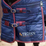 Blue quilted horse rug with Trojan branding on a blurred background