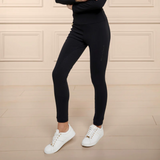 Person wearing black riding leggings and white training shoes against a beige wall.