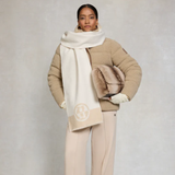 Woman wears a natural borg jacket and oversized scarf with a faux fur bag and grey background