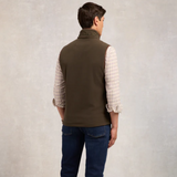 Man wearing a khaki gilet over a plaid shirt with a neutral background