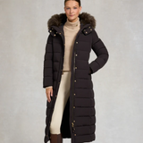 Woman wearing a long dark brown puffer coat with a fur-lined hood on a plain background