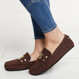 Brown loafers worn with blue jeans on a light wooden floor.