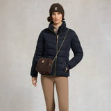 Woman wearing a navy puffer jacket, brown beanie, and carrying a brown handbag on a plain background