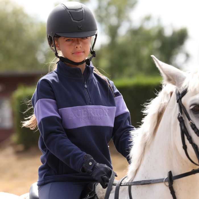 Young rider on horse wearing navy and purple sweater on blurred background