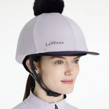 Person wearing a lilac LeMieux equestrian helmet cover with a black pom-pom on a white background