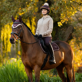 Woman riding a horse in an outdoor setting with trees and greenery.