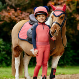 Child in equestrian gear standing next to a small pony outdoors