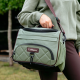 Person holding a green equestrian bag with 'LeMieux' branding outdoors.