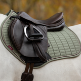 Brown leather saddle on a green quilted saddle pad with a blurred natural background