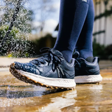 Person wearing blue running shoes with white soles splashing through water outdoors.