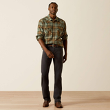 Man wearing a plaid shirt and dark jeans standing against a plain background