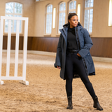 Person wearing a blue coat and black riding leggings in an indoor equestrian arena.