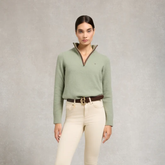 Holland Cooper Country Quarter Zip Knit Variant Colour Sage. A model wearing a sage green sweater, brown belt and cream trousers on grey background.