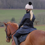 Woman rides a horse wearing a black coat in a countryside setting
