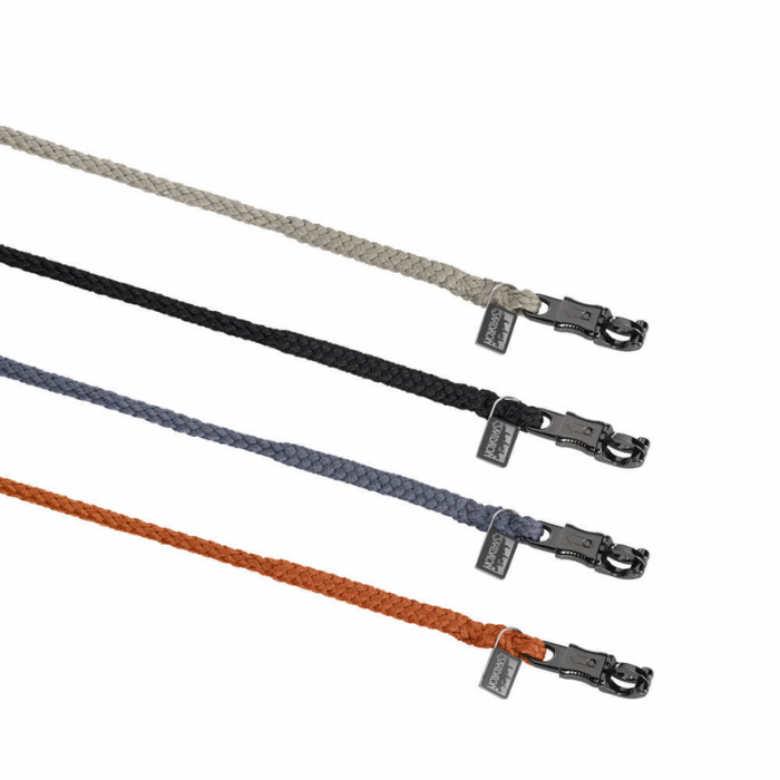 Four braided rope horse leads in light gray, black, slate blue, and rust orange, each with a dark metal lobster clasp and a small fabric brand tag, arranged diagonally on a white background.